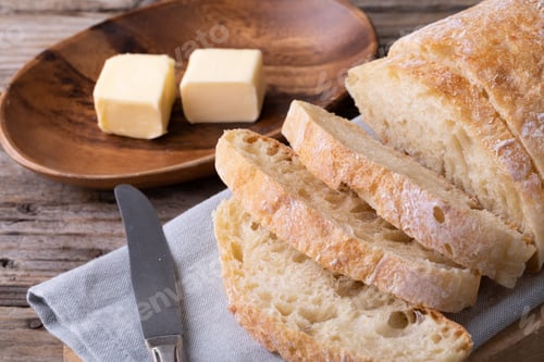 Preview: Close-up of sliced bread loaf on napkin by butter cubes in plate at table