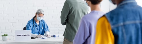 Preview: mature asian nurse in medical mask writing in vaccination center near blurred multiethnic patients,
