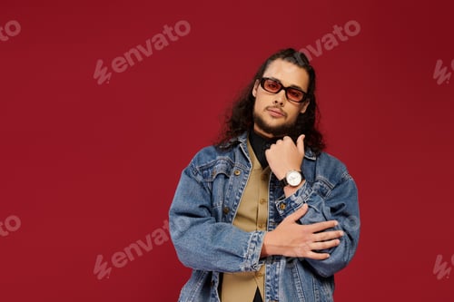 Preview: Handsome young bearded man poses confidently against a vibrant red backdrop showcasing his style