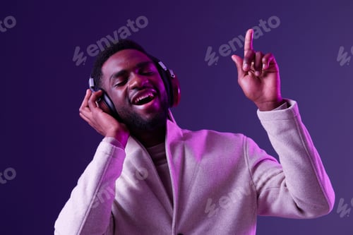 Preview: Young man enjoying music with headphones, expressing joy in a purple lit environment, conveying a