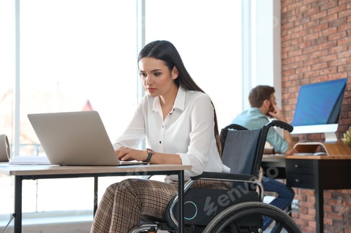 Preview: Young woman in wheelchair using laptop at workplace