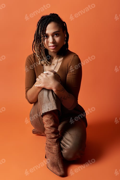 Preview: Young African American woman with braids poses stylishly in front of an orange backdrop
