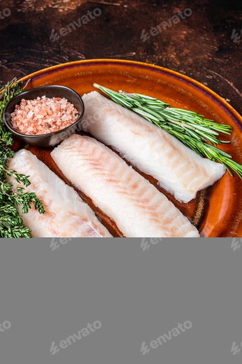 Preview: Raw Haddock loin fillet fish on rustic plate with thyme and salt. Dark background. Top view