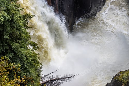 Preview: High angle view of a massive waterfall splash on a cliff above trees