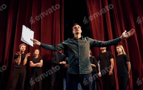 Preview: Man is practicing his role. Group of actors in dark colored clothes on rehearsal in the theater