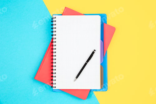 Preview: Notebooks and pen on a blue and yellow background, top view.