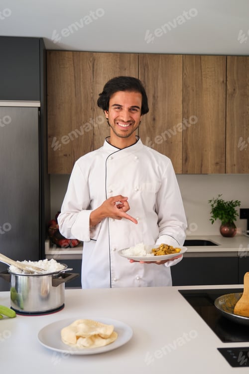 Preview: Indian chef holding plate of food in modern kitchen