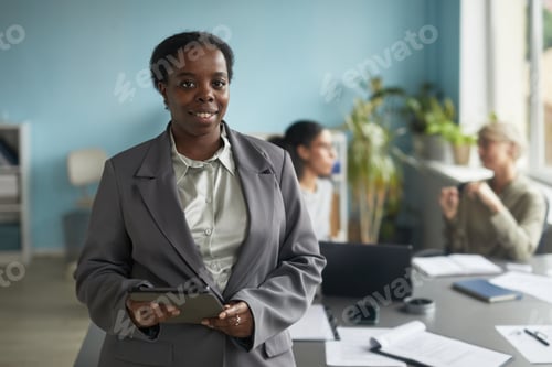 Preview: Portrait of Young Adult Black Woman Holding Tablet in Modern Office Setting