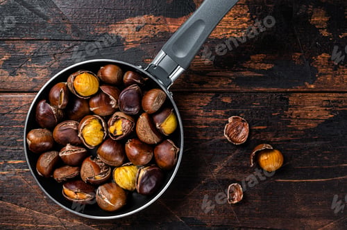 Preview: Roasted chestnuts nuts in a pan. Wooden background. Top view