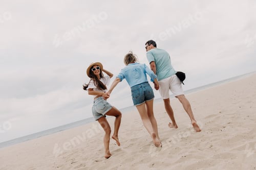 Preview: Three happy young friends spending fun time while running by the beach to the sea together