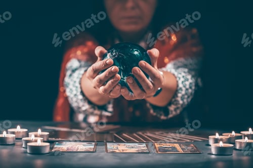 Preview: Tarot reader with tarot cards.Tarot cards face down on table near burning candles and crystal ball.