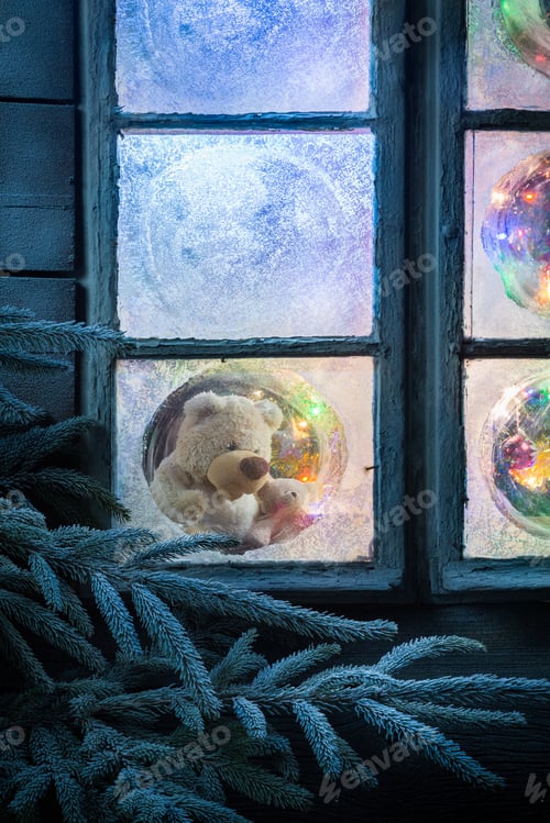 Preview: Teddy bear in frozen window for Christmas with tree and lights