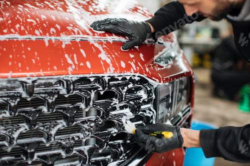 Preview: Close up photo of man hand in black protective gloves cleaning radiator grille in foam