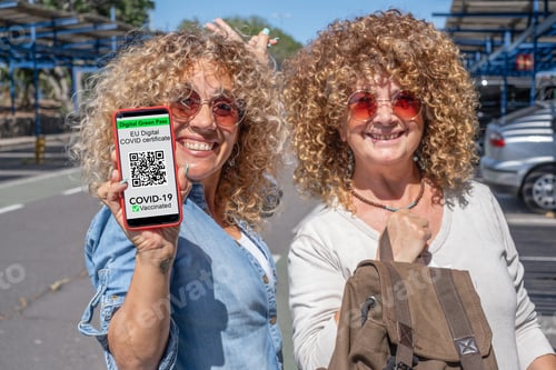 Preview: Two smiling curly women holding mobile phone with digital certificate of vaccination of covid 19