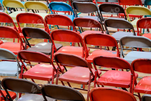 Preview: Rows of metal folding chairs of different colours, grey, red, yellow.