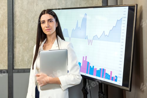 Preview: Young businesswoman standing near screen with charts