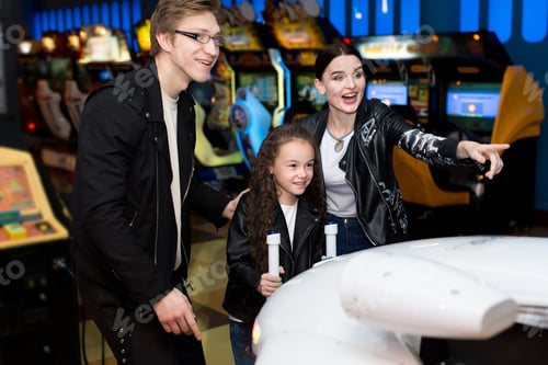 Preview: Family mother, father, daughter play arcade games on the computer machines at an amusement park