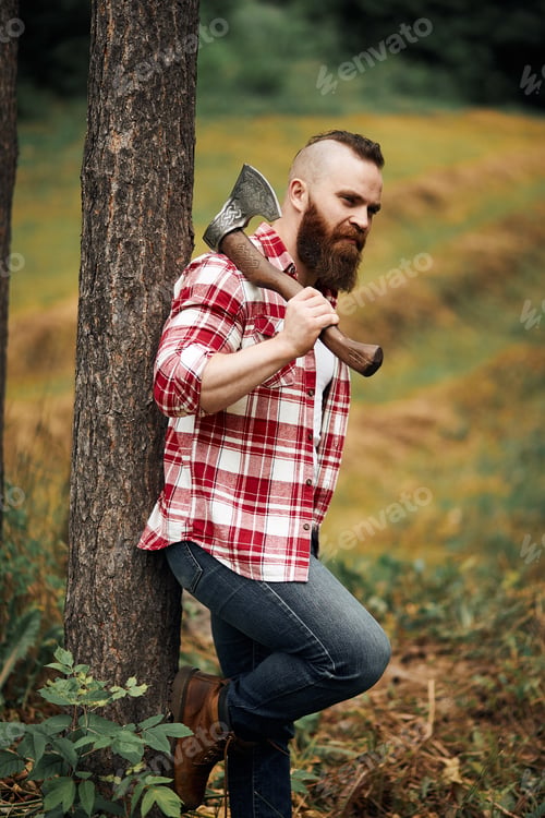 Preview: bearded lumberjack worker standing in forest with axe