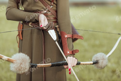 Preview: Young woman warrior with a bow pulls the bowstring with an arrow, close-up