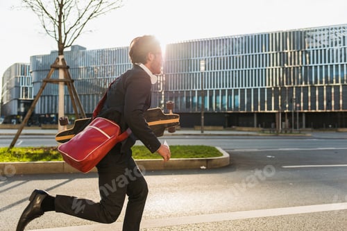 Preview: Germany, Frankfurt, Young businessman running with skateboard under his arm, using mobile phone