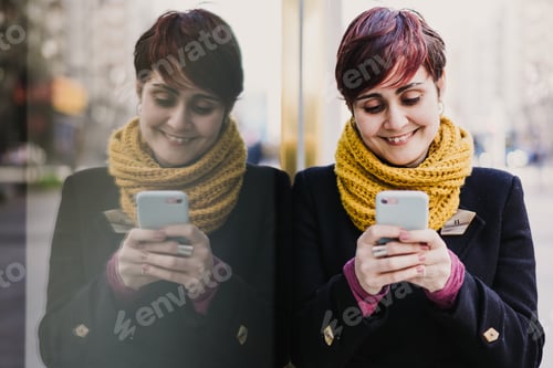 Preview: young beautiful woman using mobile phone outdoors. Reflection on glass. Technology and lifestyle