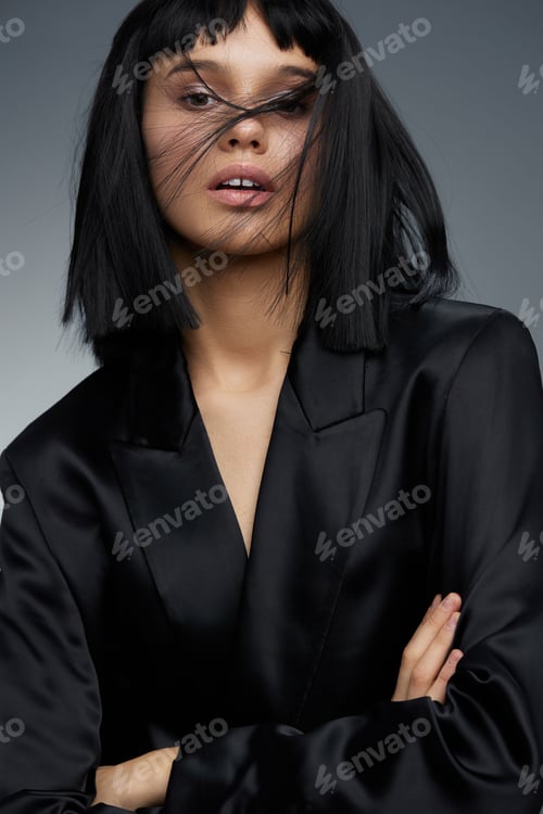 Preview: Blackhaired woman in a black suit poses confidently with arms crossed against a gray background