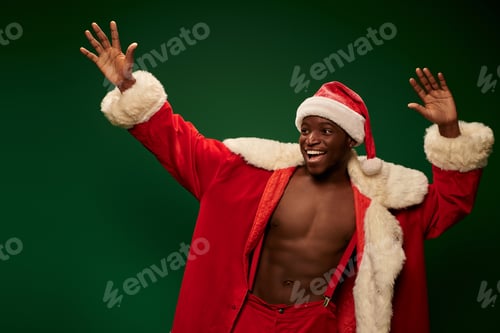 Preview: joyful african american guy in christmas costume on shirtless body waving hands on green backdrop