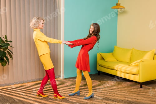 Preview: side view of pretty smiling women in retro clothes holding hands at colorful apartment, doll house