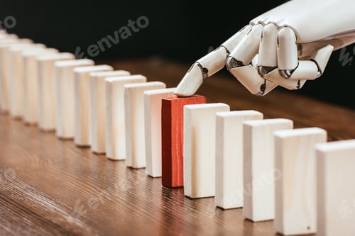 Preview: selective focus of robotic hand picking red wooden brick from row of blocks on desk