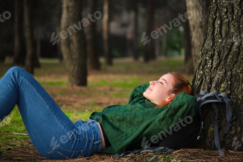 Preview: Redhead young woman resting lying under tree in forest.