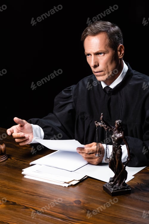 Preview: judge in judicial robe sitting at table and holding paper isolated on black