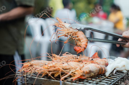 Preview: Grilling shrimp on a barbecue. Someone in a red shirt is using tongs to flip the shrimp, smoke