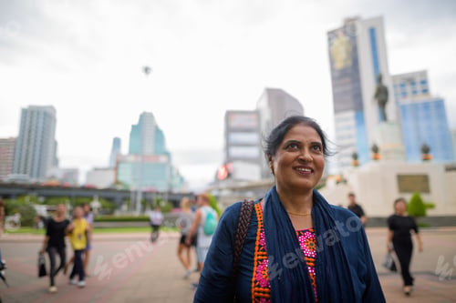 Preview: Mature beautiful Indian woman smiling and thinking in city