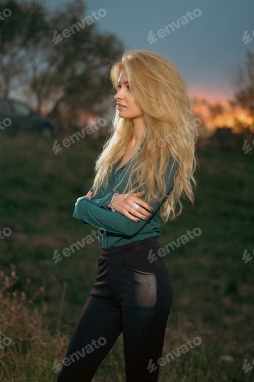 Preview: Woman stands alone on grassy hill during sunset with blurred background