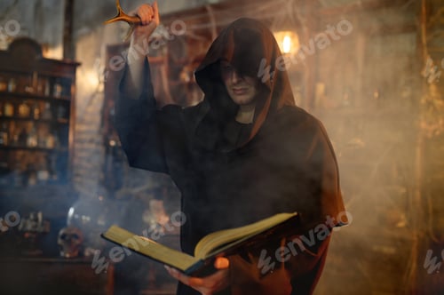 Preview: Male exorcist in black hood holds book of spells