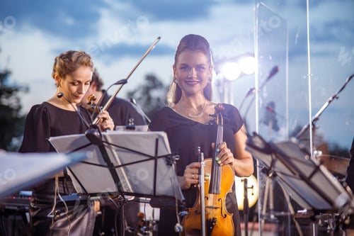 Preview: Cheerful woman violin player playing in orchestra outdoors