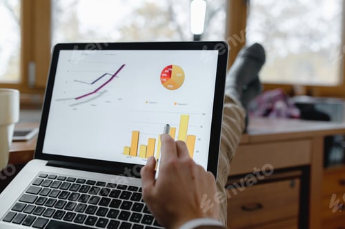 Preview: Businessman sitting on a chair with his legs on the desk and analysing a business chart