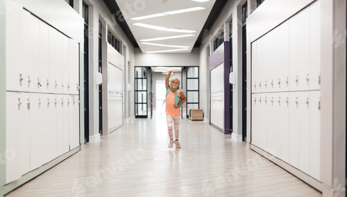 Preview: Full length of caucasian elementary schoolgirl with arms raised running in school corridor