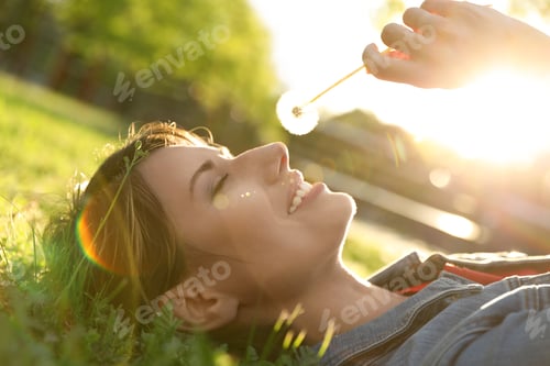 Preview: Young woman with dandelion in park on sunny day. Allergy free concept