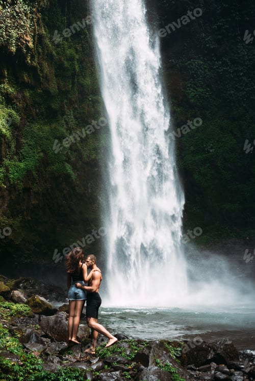Preview: A couple in love on a waterfall. A man of athletic build kisses a beautiful girl at the waterfall