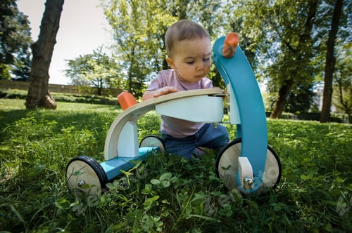 Preview: Curious toddler exploring a colorful toy outdoors on a sunny day.