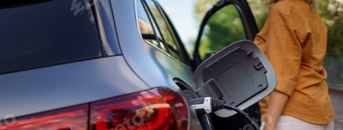 Preview: Woman waiting while electric car charging, close-up.