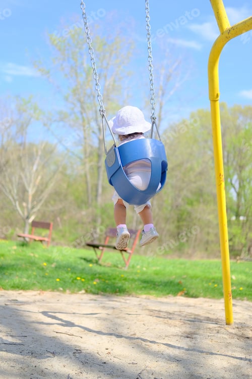 Preview: Cute toddler girl in swing at park on a nice sunny summer day