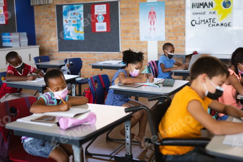Preview: Group of students wearing face masks studying while sitting on their desks at elementary school