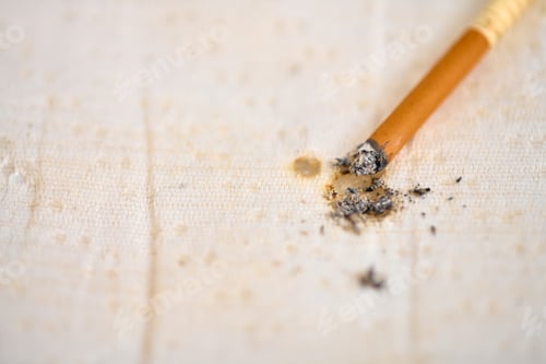 Preview: Burned cigarette on beige fabric surface