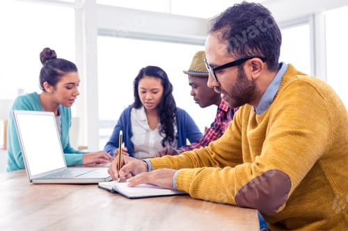 Preview: Business man writing in book while sitting with colleagues in creative office