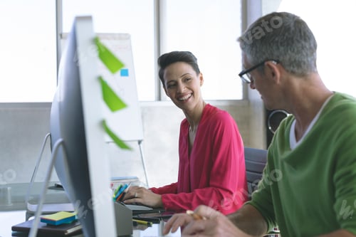 Preview: Side view of Multi-ethnic business people discussing over computer at desk in modern office