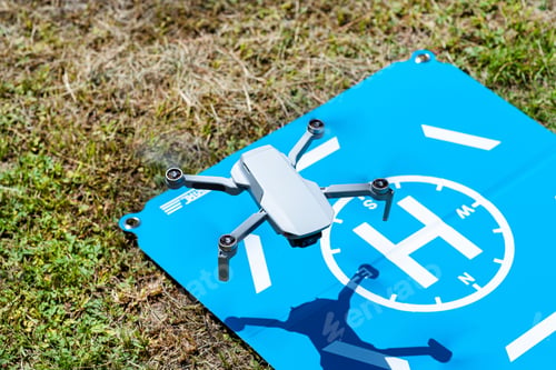 Preview: The drone hovers over the blue landing pad on the grass, the plastic propellers are on