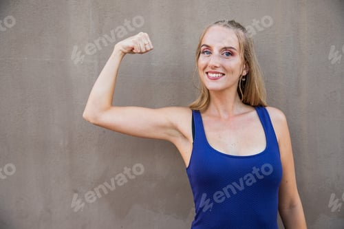 Preview: A young woman with her bicep raised, strength concept, model isolated on a grey background