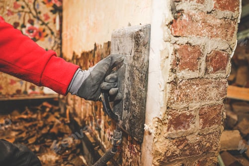 Preview: Hands of a young caucasian guy removes retro wallpaper using a steamer machine in an old house.